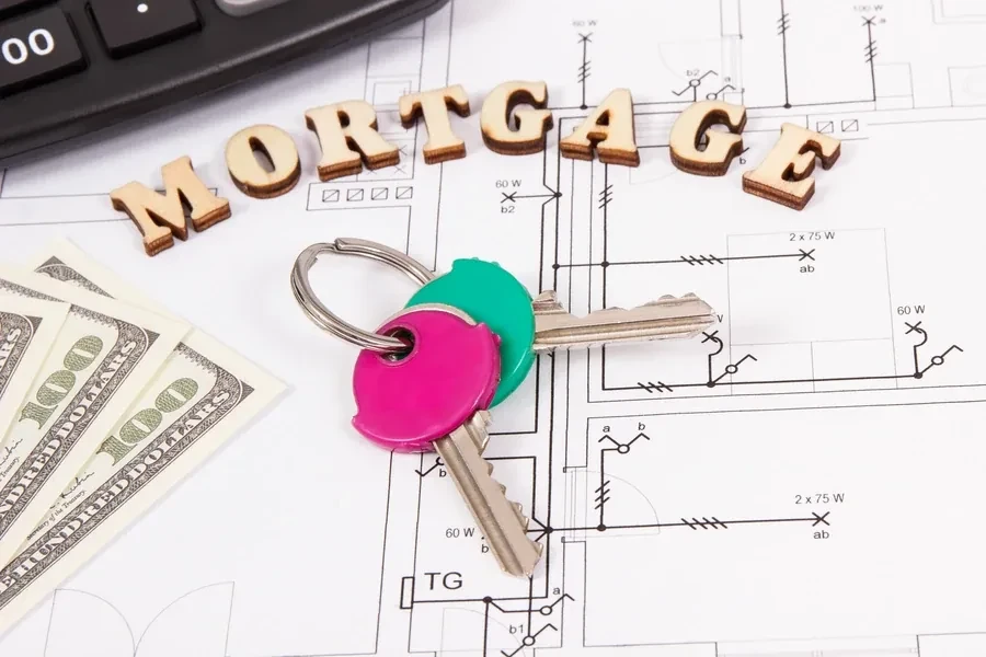 Wooden letters spelling MORTGAGE above keys, cash and a blueprint with a calculator