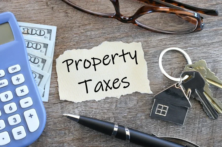 A property taxes note on a desk with keys, calculator, cash, glasses and a pen