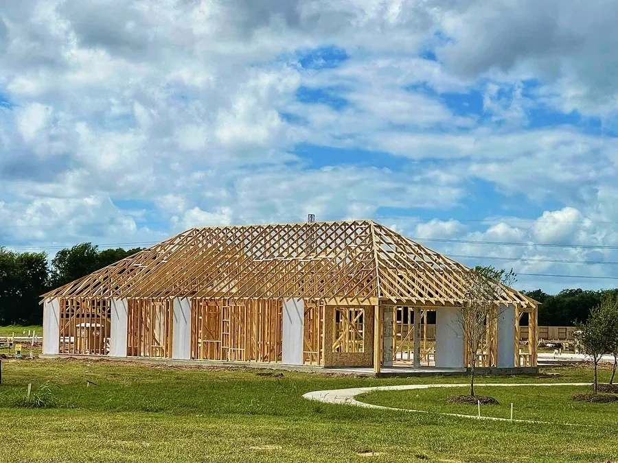 Wood-framed new construction house in an open grass field under a cloudy sky