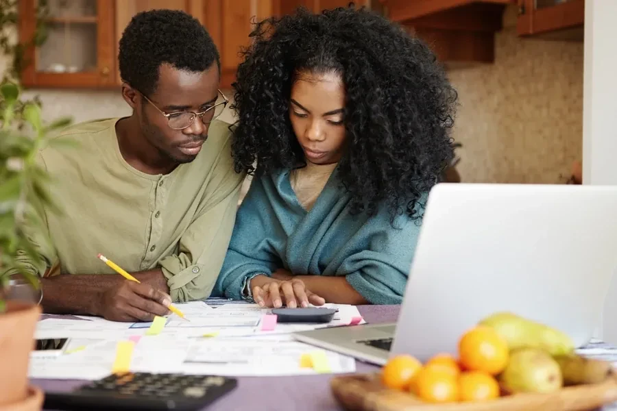 Couple working through bills and a calculator at a kitchen table with a laptop